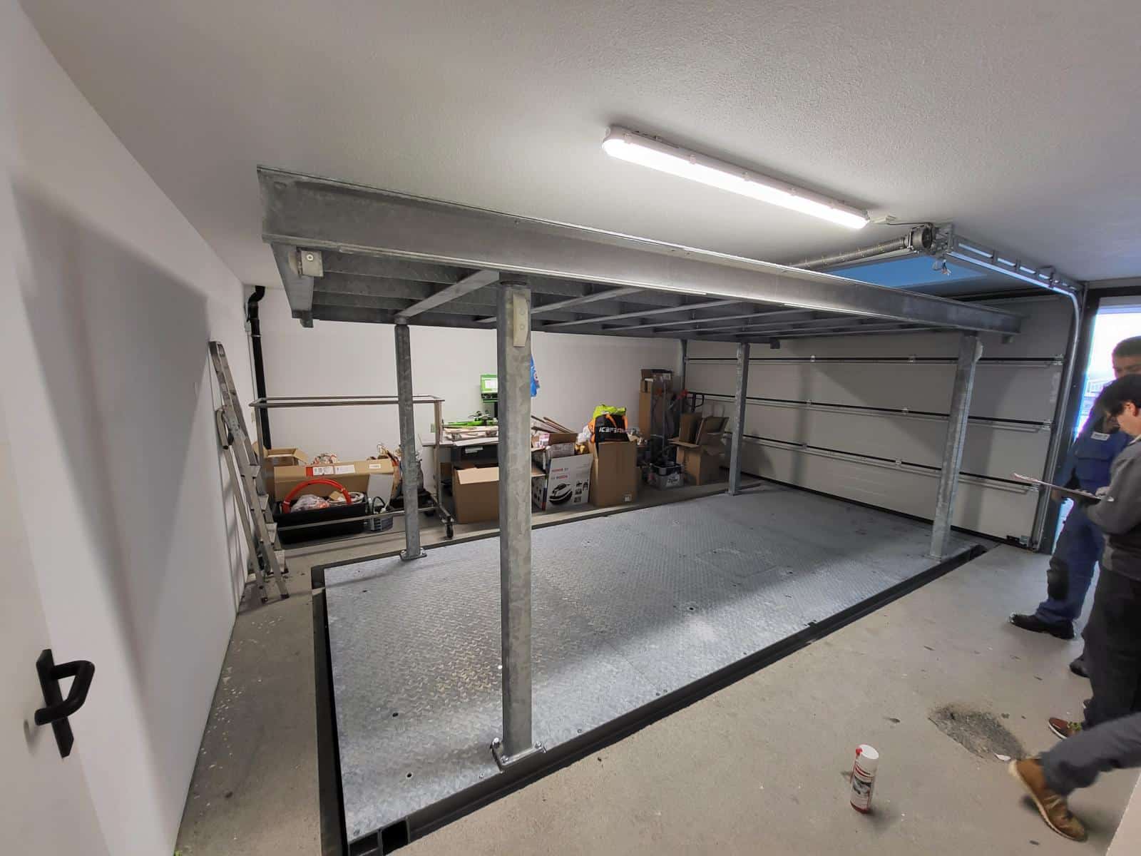 Eine Garage mit zwei Personen, die neben einem Schwerlasthubtisch stehen.
